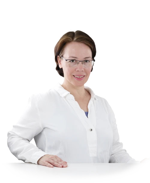 Rosa Sanchez steht in einer weißen Blusentunika an einem Tisch. Sie hat die Hände auf die Tischplatte gelegt und lächelt in die Kamera.