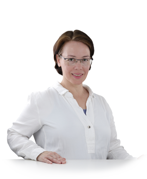 Rosa Sanchez steht in einer weißen Blusentunika an einem Tisch. Sie hat die Hände auf die Tischplatte gelegt und lächelt in die Kamera.