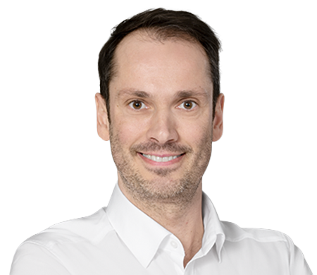 Bernhard Maier smiles at the camera. He is wearing a white shirt with an open collar. He has short, dark brown hair and a slight shadow of a beard.