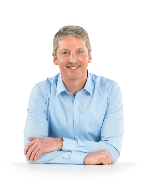 Thomas Kern is standing at a table in a white shirt. He is leaning relaxed over a table and leaning on his folded arms. He smiles friendly into the camera.