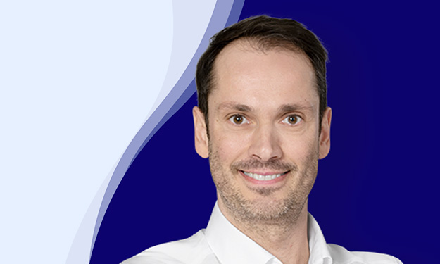 Bernhard Maier smiles at the camera. He is wearing a white shirt with an open collar. He has short, dark brown hair and a slight shadow of a beard. The background has a modern design with curved waves in dark blue, white and light blue.