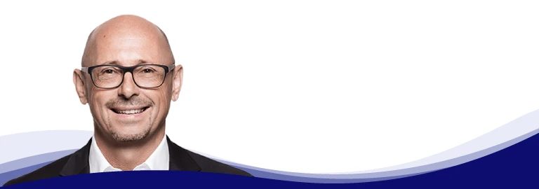 Günther Rossdeutscher, Managing Partner at asecos, looks friendly into the camera. He is wearing dark glasses, a white shirt and a dark jacket. He is bald with a short beard.