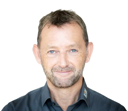 Achim Angel, Managing Director of KiM GmbH - Member of 4PACE, smiles friendly into the camera. He has short brown hair, a short beard and is wearing a dark gray shirt with a slightly open collar. A curved wave shape in white, light blue and dark blue can be seen in the background, giving the picture a modern design.