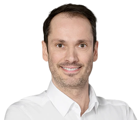 Bernhard Maier smiles at the camera. He is wearing a white shirt with an open collar. He has short, dark brown hair and a slight shadow of a beard.