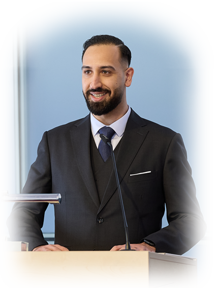 Navid Sheikh stands at the lectern in a suit