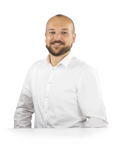 Michael Binder stands behind a table in a white shirt and looks into the camera with a smile.