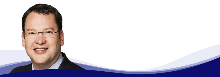 Dirk Amann, CTO Managing Director at i.safe MOBILE, looks into the camera with a smile. He is wearing rimless glasses, a light blue shirt and a dark jacket. He has short, dark brown hair and a natural complexion.