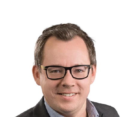 Dominik Fimberger, responsable du marketing et du e-commerce chez Weyland Steiner, sourit à la caméra. Il porte des lunettes à monture sombre, une chemise bleu clair à col ouvert et une veste grise par-dessus. Ses cheveux sont courts et bruns et il ne porte pas de barbe.