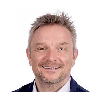 Holger Geck, directeur du marketing et de la gestion des données produits chez Gust. Alberts, sourit à la caméra. Il a les cheveux courts, blond grisâtre et une courte barbe. Il porte une chemise blanche et une veste sombre. En arrière-plan, on peut voir une forme de vague incurvée en blanc, bleu clair et bleu foncé.