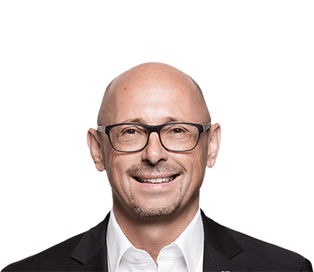 Günther Rossdeutscher, associé gérant d'asecos, regarde aimablement la caméra. Il porte des lunettes noires, une chemise blanche et une veste sombre. Il est chauve avec une courte barbe.