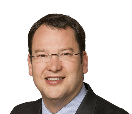 Dirk Amann, CTO Managing Director chez i.safe MOBILE, regarde la caméra en souriant. Il porte des lunettes sans monture, une chemise bleu clair et une veste sombre. Il a les cheveux courts, châtain foncé et un teint naturel.