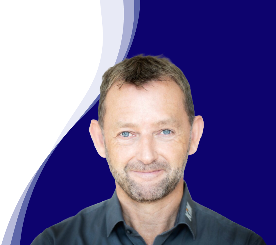 Achim Angel, directeur de KiM GmbH - Member of 4PACE, sourit aimablement à la caméra. Il a les cheveux bruns courts, une courte barbe et porte une chemise gris foncé avec un col légèrement ouvert. En arrière-plan, une forme ondulée incurvée en blanc, bleu clair et bleu foncé confère à la photo un design moderne.