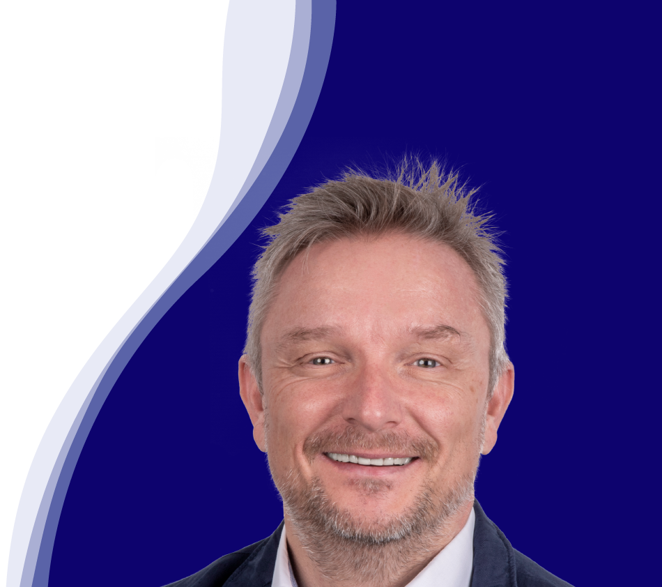 Holger Geck, directeur du marketing et de la gestion des données produits chez Gust. Alberts, sourit à la caméra. Il a les cheveux courts, blond grisâtre et une courte barbe. Il porte une chemise blanche et une veste sombre. En arrière-plan, on peut voir une forme de vague incurvée en blanc, bleu clair et bleu foncé.
