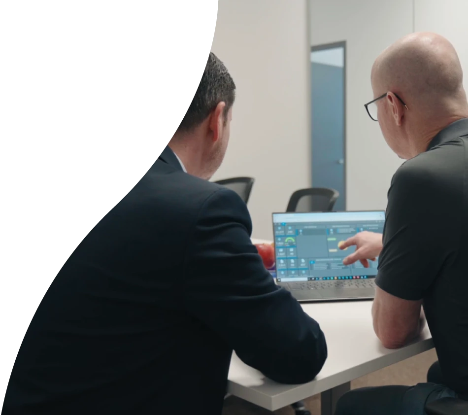 Deux hommes sont assis dans une salle de réunion d'un bureau, dos à la caméra. Sur la table devant vous se trouve un ordinateur portable avec le tableau de bord de crossbase ouvert. L'homme à droite montre l'écran et porte des lunettes.